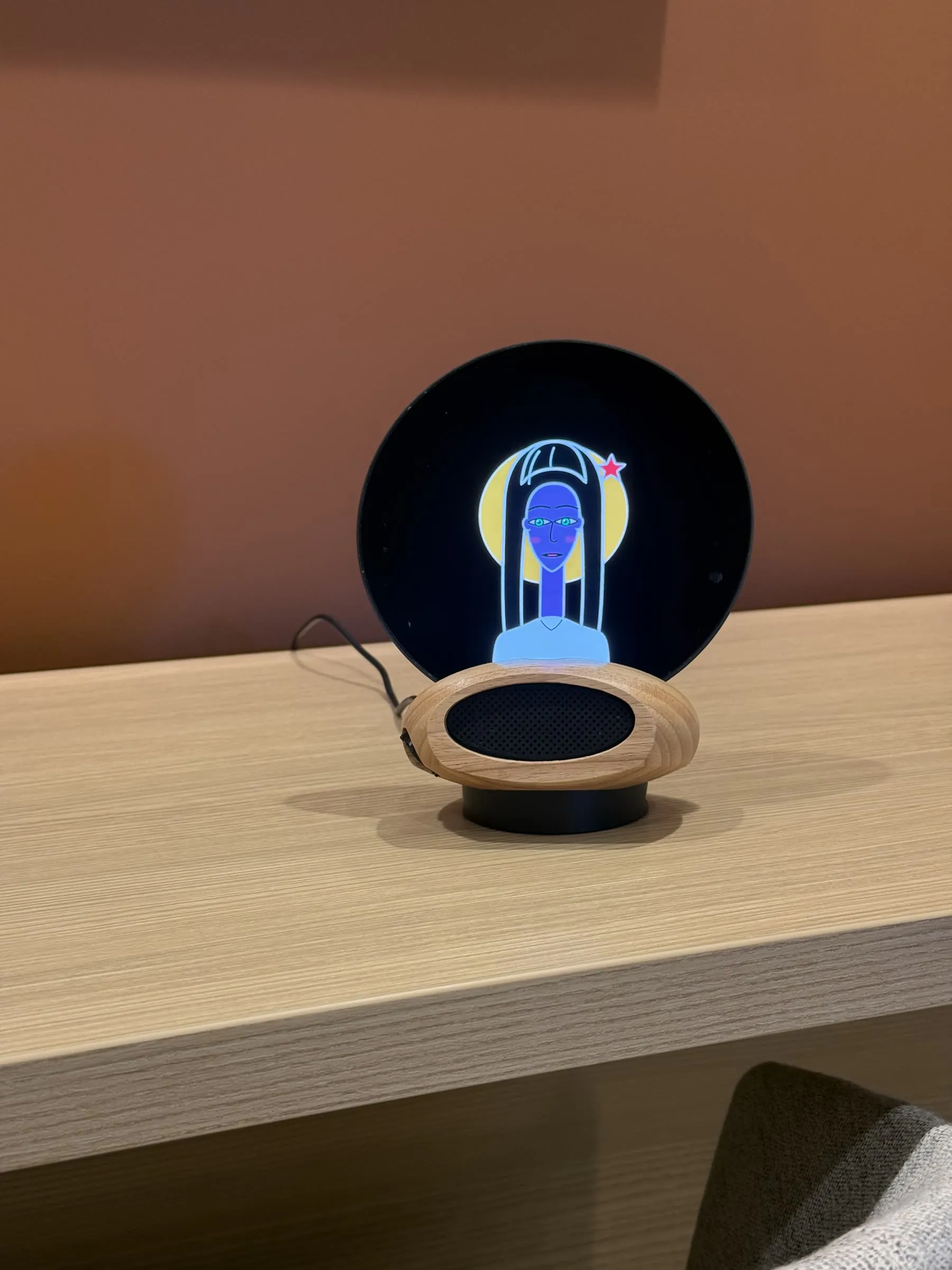 Morph on a desk against a terracotta wall, a blue character with a yellow halo on the glass